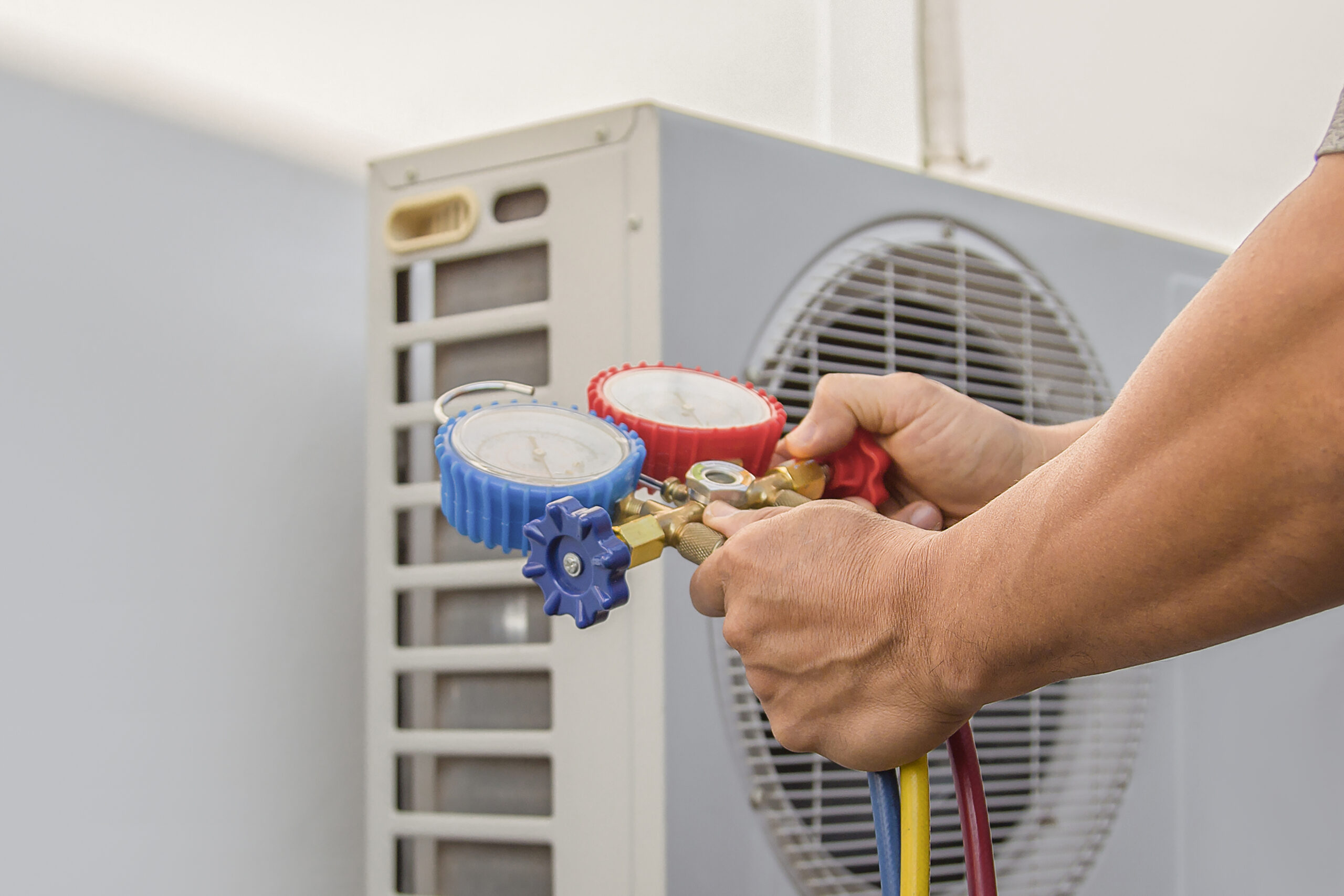 Air conditioning, HVAC service technician using gauges to check refrigerant and add refrigerant.